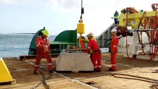 ADCP on ship deck at sea with crane, four people wearing helmets and safery gear