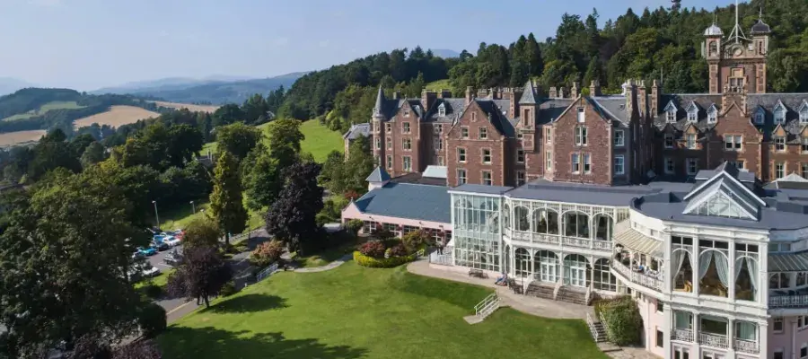 panoramic exterior view of Crieff Hydro Hotel with mountains, trees, fields and blue sky in the background