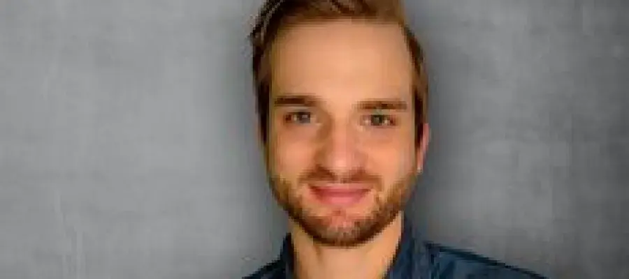 Dr Tim Ballweg headshot, smiling wearing dark shirt with grey background