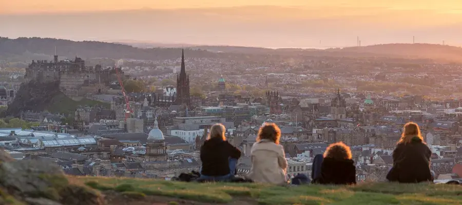 Four undergraduate engineering students sitting on top of Salisbury Crags watching the sunset over Edinburgh