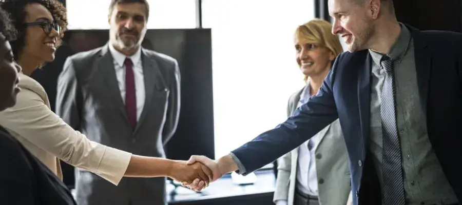 Two people shaking hands whilst other watch on, within an office environment