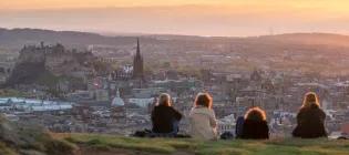 Four undergraduate engineering students sitting on top of Salisbury Crags watching the sunset over Edinburgh