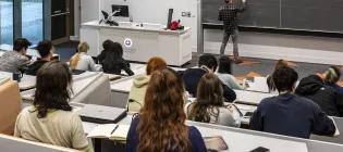 Students sitting in a lecture theatre, with a lecturer writing on the blackboard.