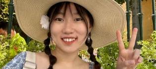 Jie Chen wearing straw hat and dress smiling and showing peace sign