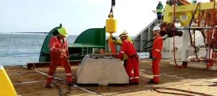 ADCP on ship deck at sea with crane, four people wearing helmets and safery gear