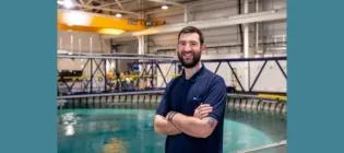 Callum Guy standing with arms crossed and smiling in front of the FloWave ocean and tidal testing facility water tank