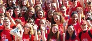 Large group of students in red t-shirts smiling and cheering together