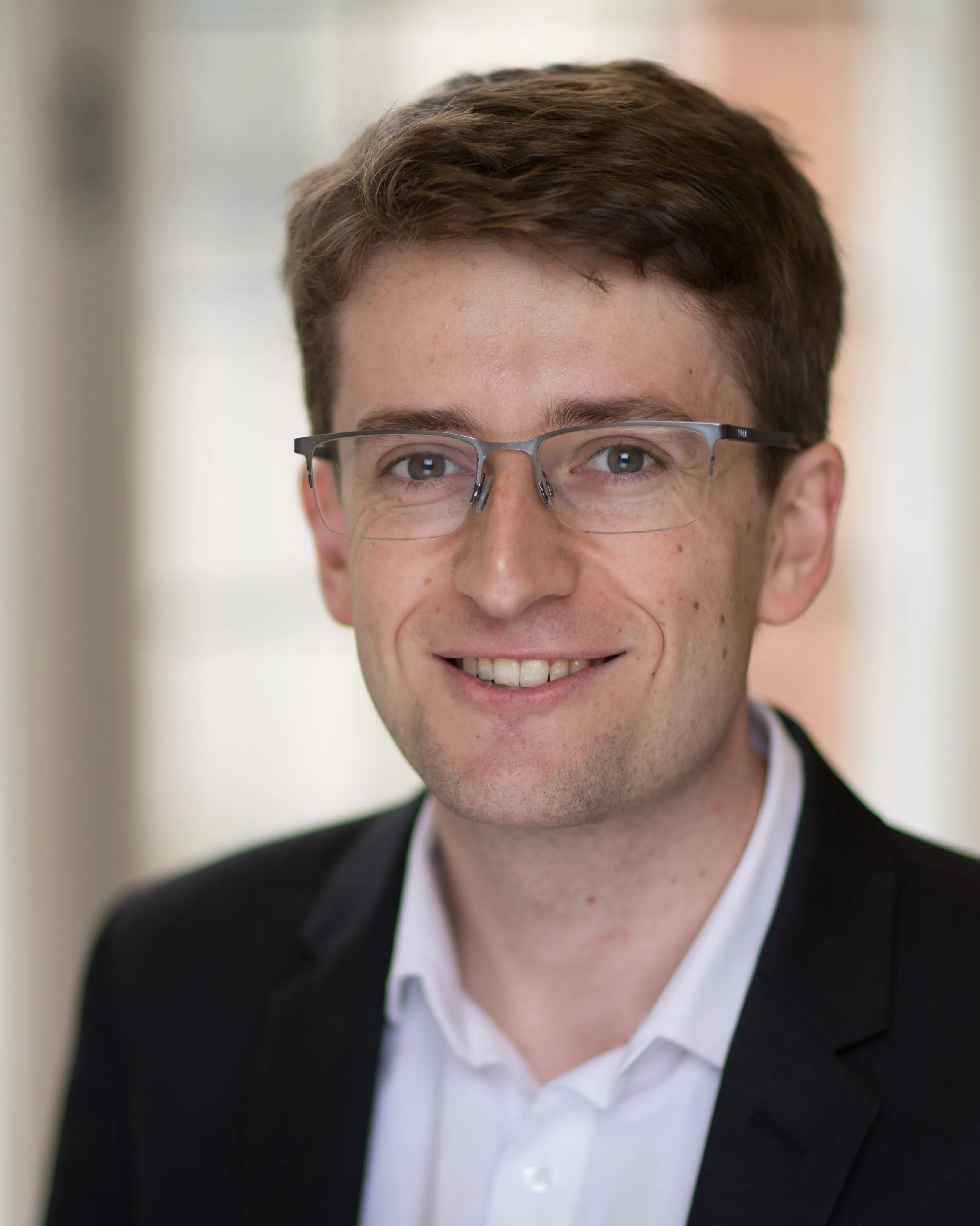 Thomas Morstyn headshot, smiling, wearing a dark suit and white shirt