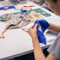 Over the shoulder photo of a woman sewing a patch on a blue square