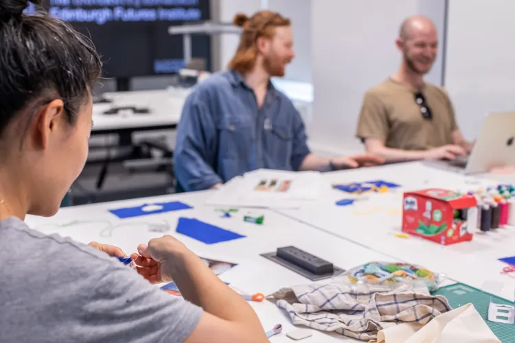 photo of two people talking in a sewing workshop while one person sews