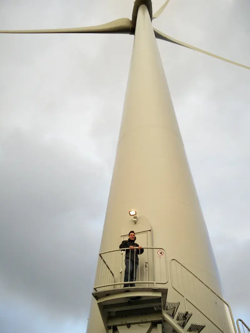 Rhodri Hawkins standing at the top of access stairs at the foot of a giant wind turbine