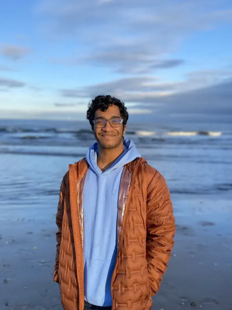 Mukhil Ramesh standing on a beach with sea and waves in the background