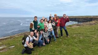 IDCORE group shot standing beside the orkney coastline, grass, cliffs and sea in the background