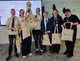 Secondary school pupils in uniform celebrating winning the NXP drone challenge with trophy with two girls holding the trophy aloft