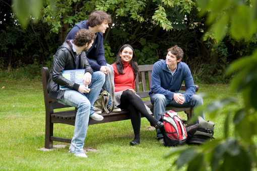 undergraduate students chatting and smiling on a park bench