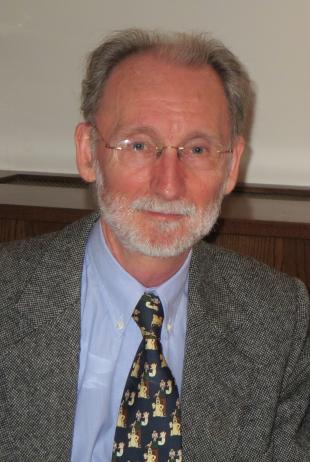 Atholl Hay, smiling portrait photograph, spectacles, grey hair and beard, wearing a grey woolen suit, blue shirt and patterned tie