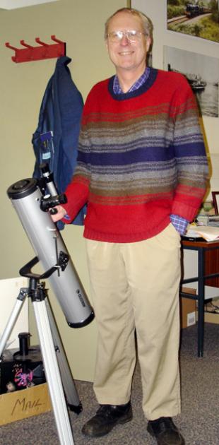 Professor Jim Hough in a red, blue and grey jumper, standing with telescope
