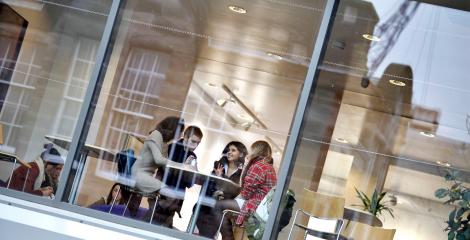 Students in discussion around a table, photo taken from outside building, looking through large glass windows